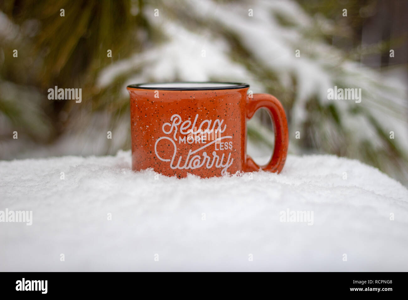 Hot mug with steam rising relax more worry less message surrounded by snowy scene and icy pine branches in winter background, holiday stress keep calm Stock Photo
