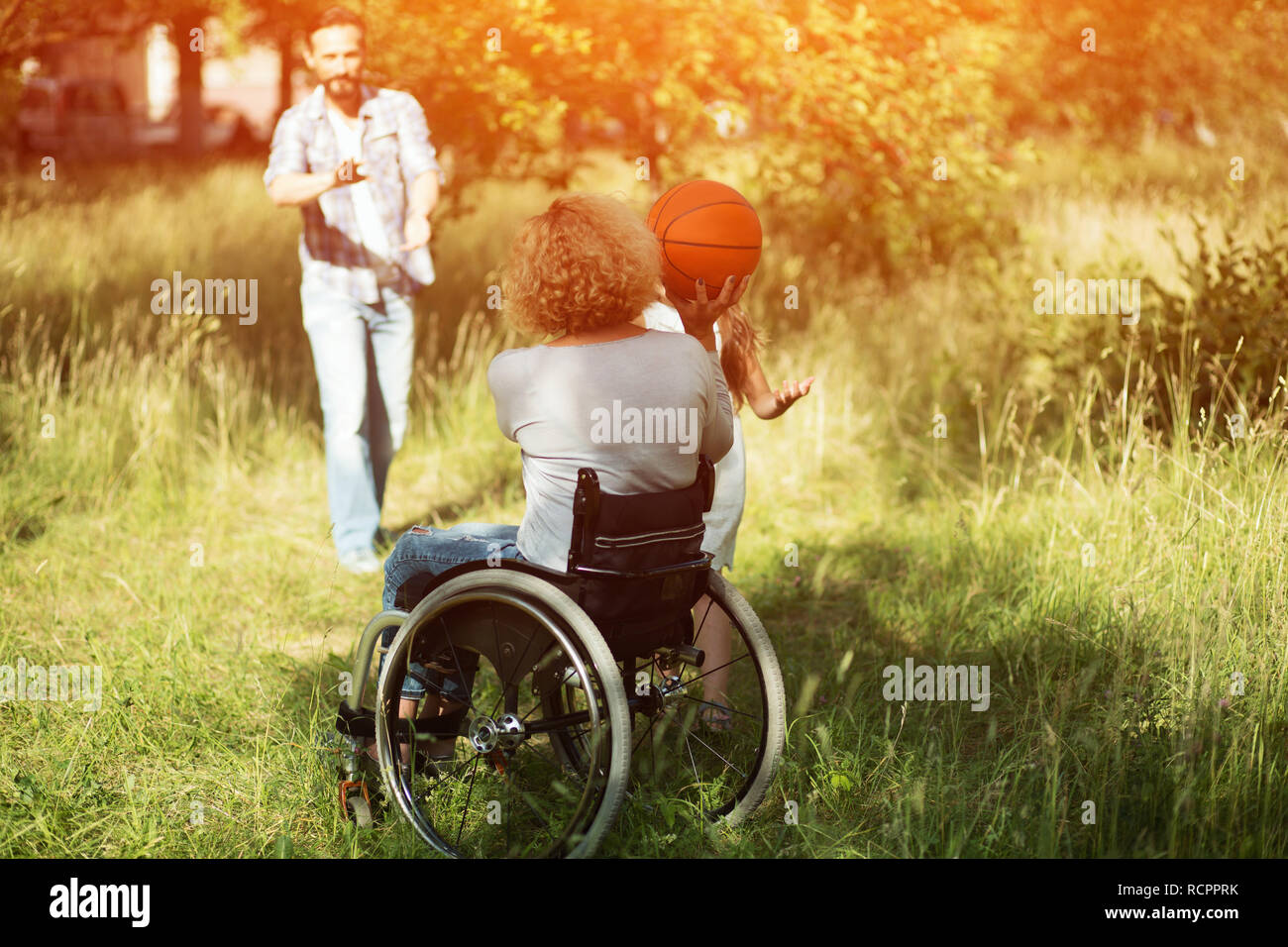 Woman in wheelchair plays with ball with her family outdoors Stock Photo