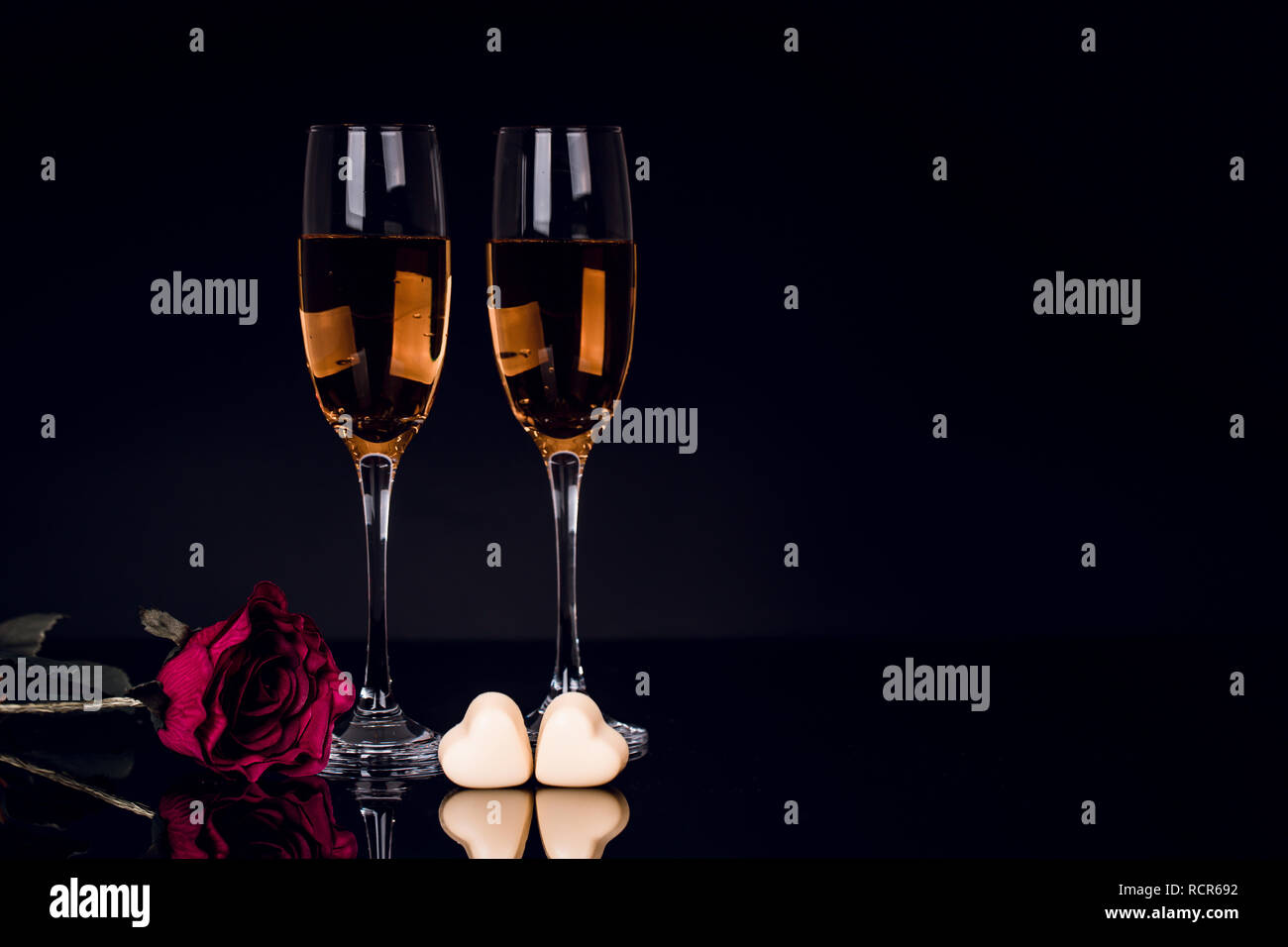 Two glasses of champagne, rose and two heart shape chocolates on black background with lights in the background. Love, Valentines day concept Stock Photo