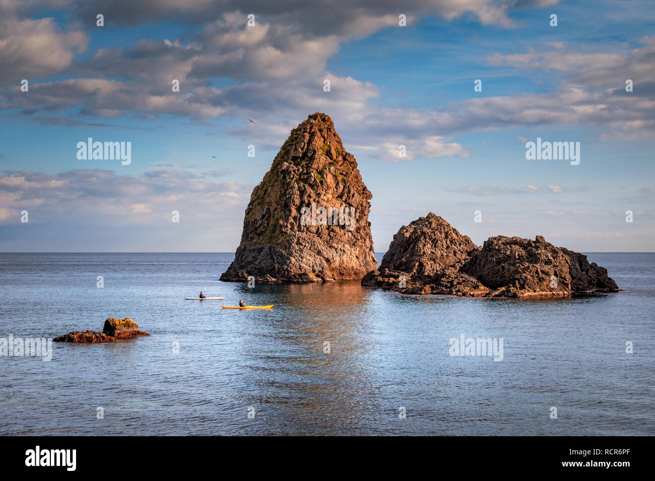 Two guys canoeing close the sea stacks of Aci trezza during a sunny winter day, Sicily, Italy Stock Photo