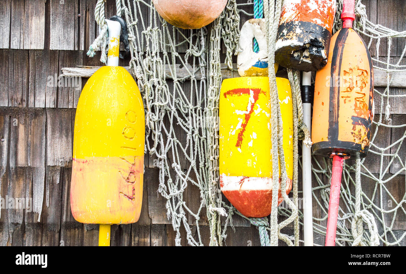 colorful lobster buoys with fishing nets hanging on a weathered shingle exterior wall in Massachusetts Stock Photo