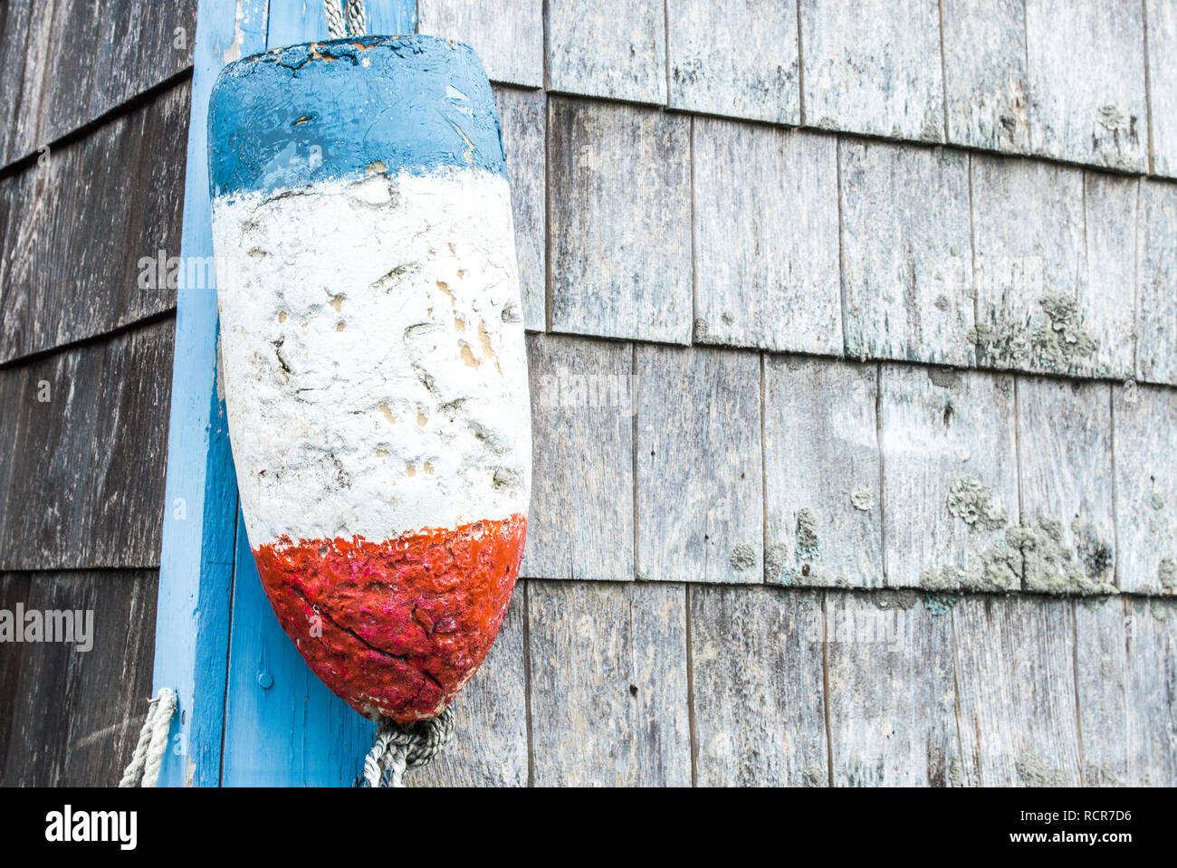 a battered red, blue and white lobster buoy hanging on the outside of a weathered fishing shack with copy space Stock Photo
