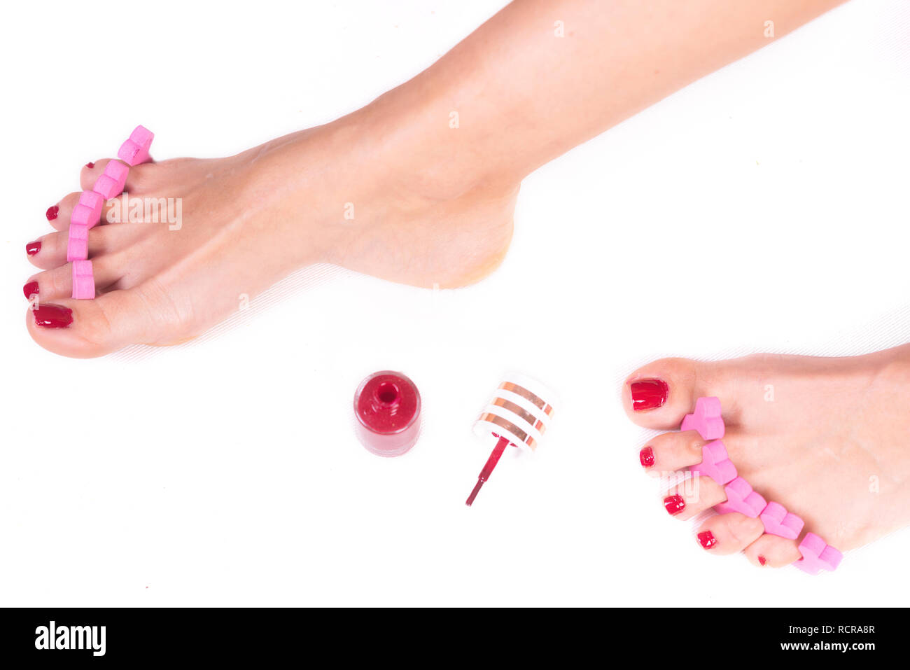 applying pedicure to woman's feet with red toenails, in pink toe separators, on white isolated background . Stock Photo