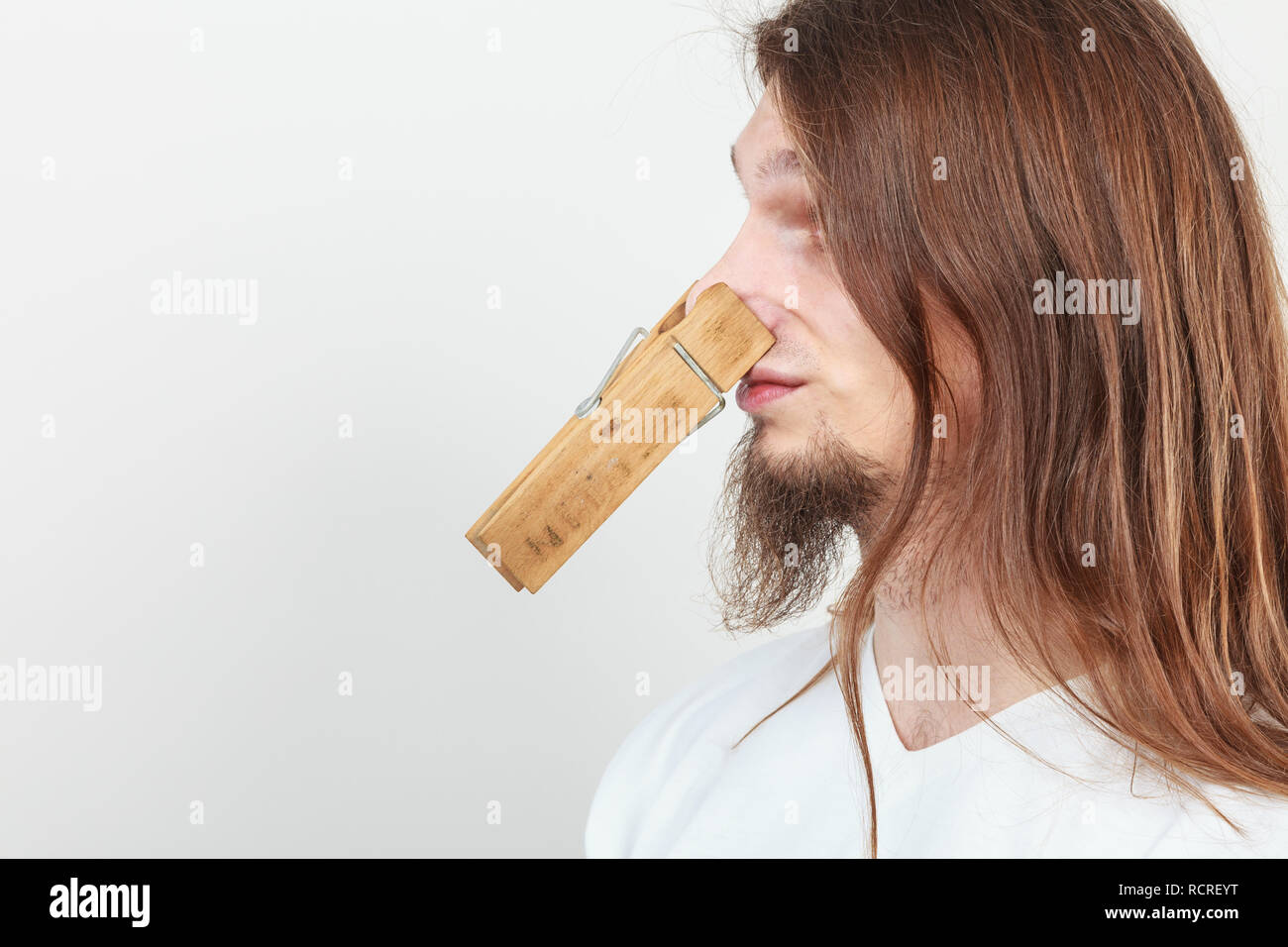 Man with clothespin clip peg on his nose. Young long haired guy feeling