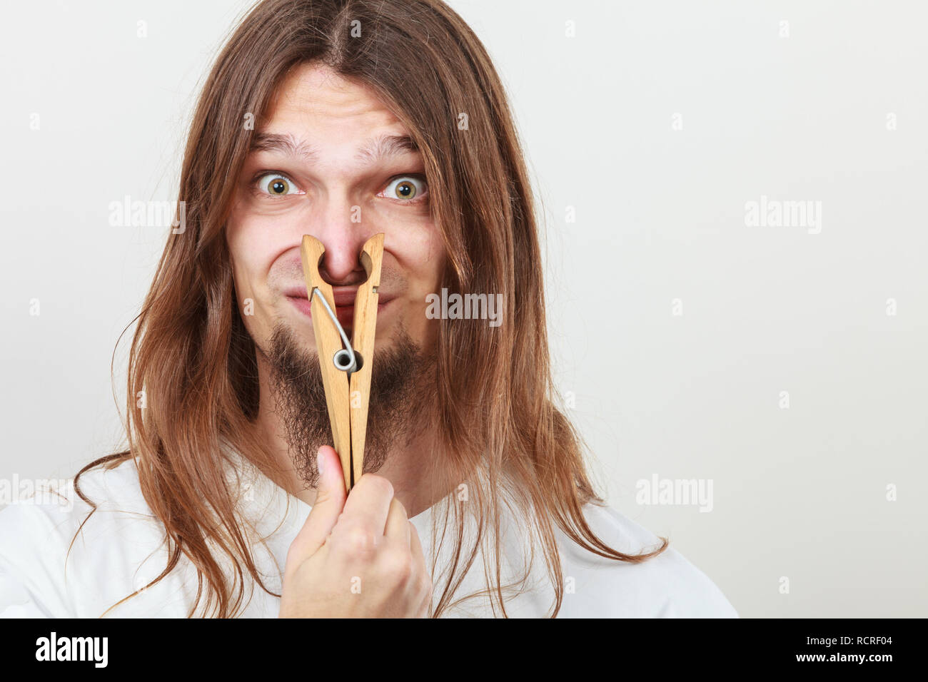 Man with clothespin clip peg on his nose. Young long haired guy feeling