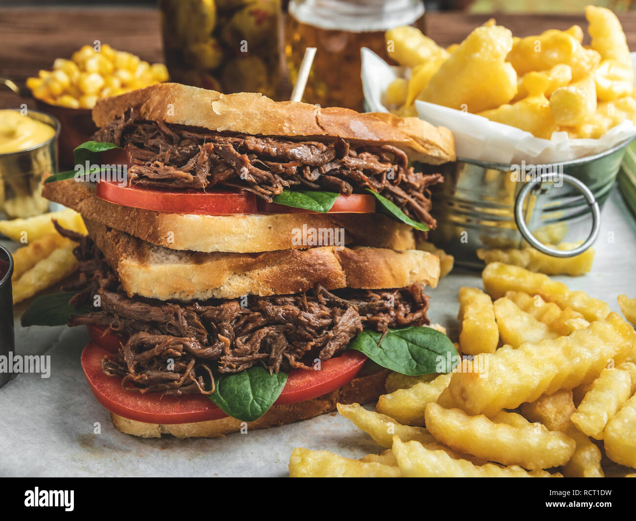 Beef sandwich pulled , barbeque, toast, french fries, sauce, corn on a wooden tray Stock Photo