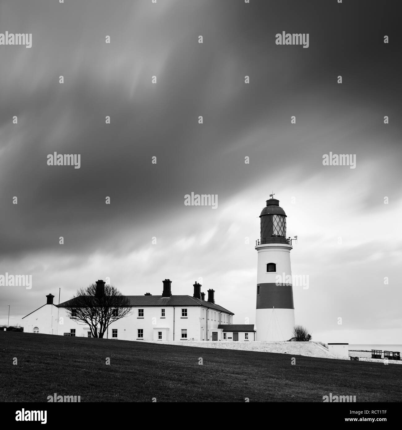 A wet & windy winter sunrise, a brief glimse of the sun lights up the clouds before dark storm clouds quickly follow engulfing the lighthouse Stock Photo