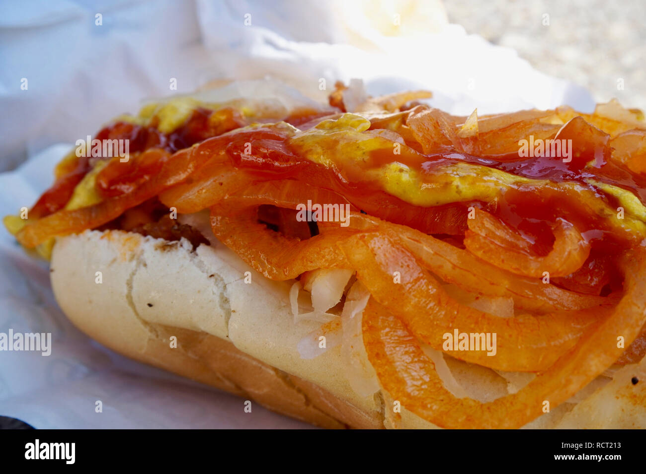 Hot dog close up smothered in ketchup, mustard, onion topping, showing the hot dog bun. Nathan's Famous hot dog, Coney Island, NY. Stock Photo