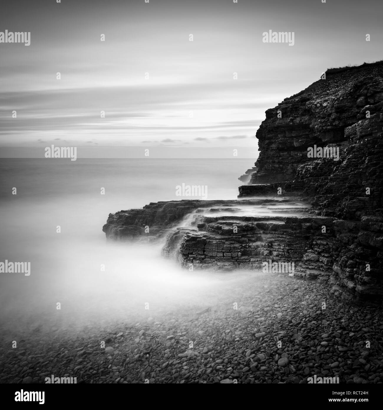 Wonderful ambient light created conditions for this long exposure of the cliffs, pebble beach and the streams of cascading water at Souter Lighthouse Stock Photo