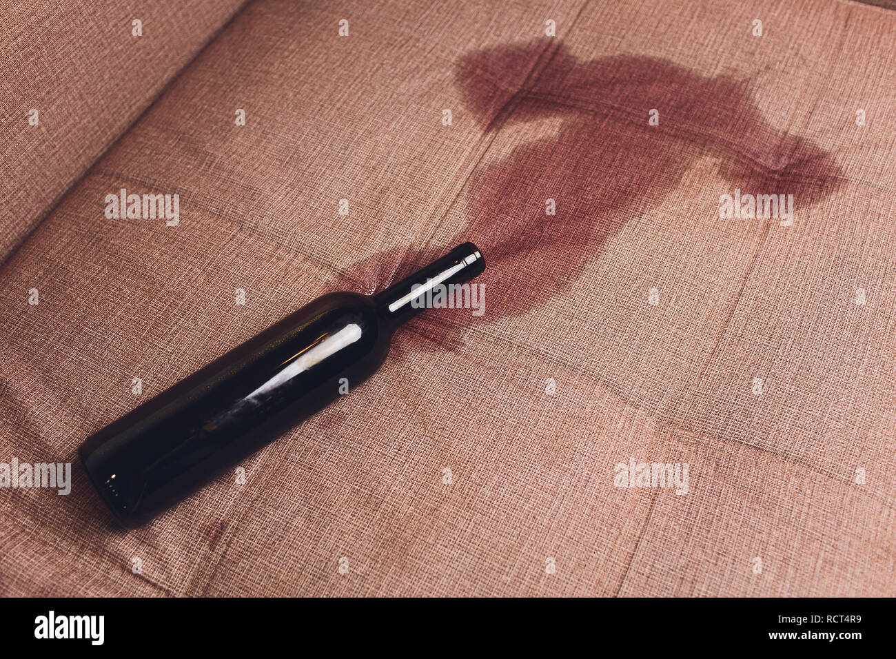 Red wine spilled on a brown couch sofa. dark bottle of red wine dropped