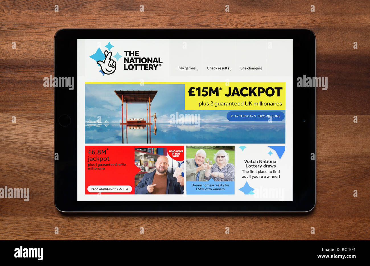 The website of the National Lottery is seen on an iPad tablet, which is resting on a wooden table (Editorial use only). Stock Photo