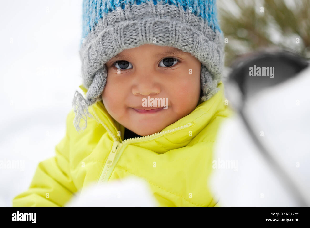 Cute Latino toddler smiling while playing in the snow during winter and wearing a knit hat. Stock Photo