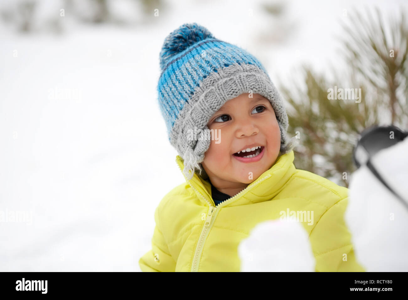 Laughing toddler boy wearing winter clothes in a snow covered mountain. Stock Photo