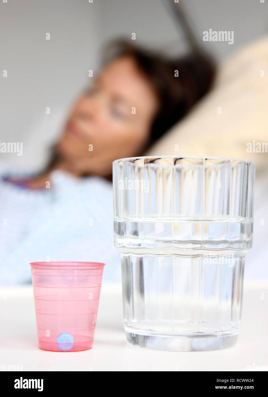 Patient in a hospital bed, medicine and a glass of water on the bedside