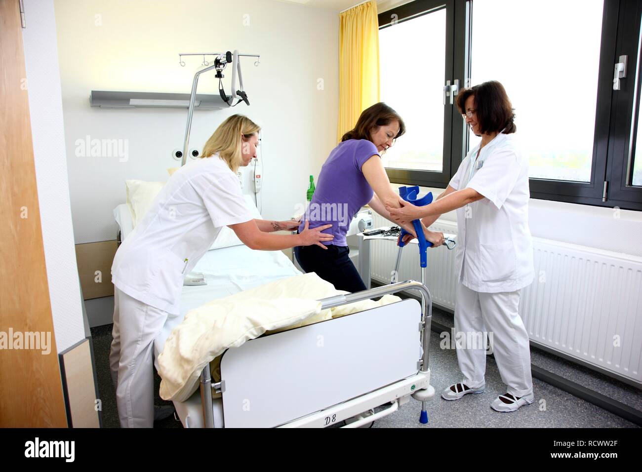 Nurses assisting a patient trying to walk with walking aids, mobilisation after an operation in a hospital Stock Photo
