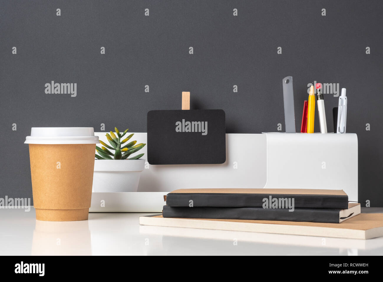 modern office stationery on white table and dark grey wall.pencil,ruler,pen,pencil box,coffee cup and blackboard with plant.Mock up paper note for dis Stock Photo