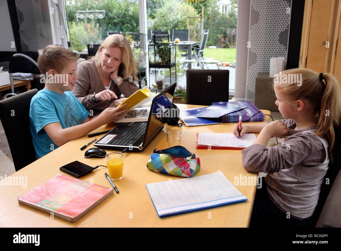 Siblings doing their homework in the living room, their mother is helping them Stock Photo