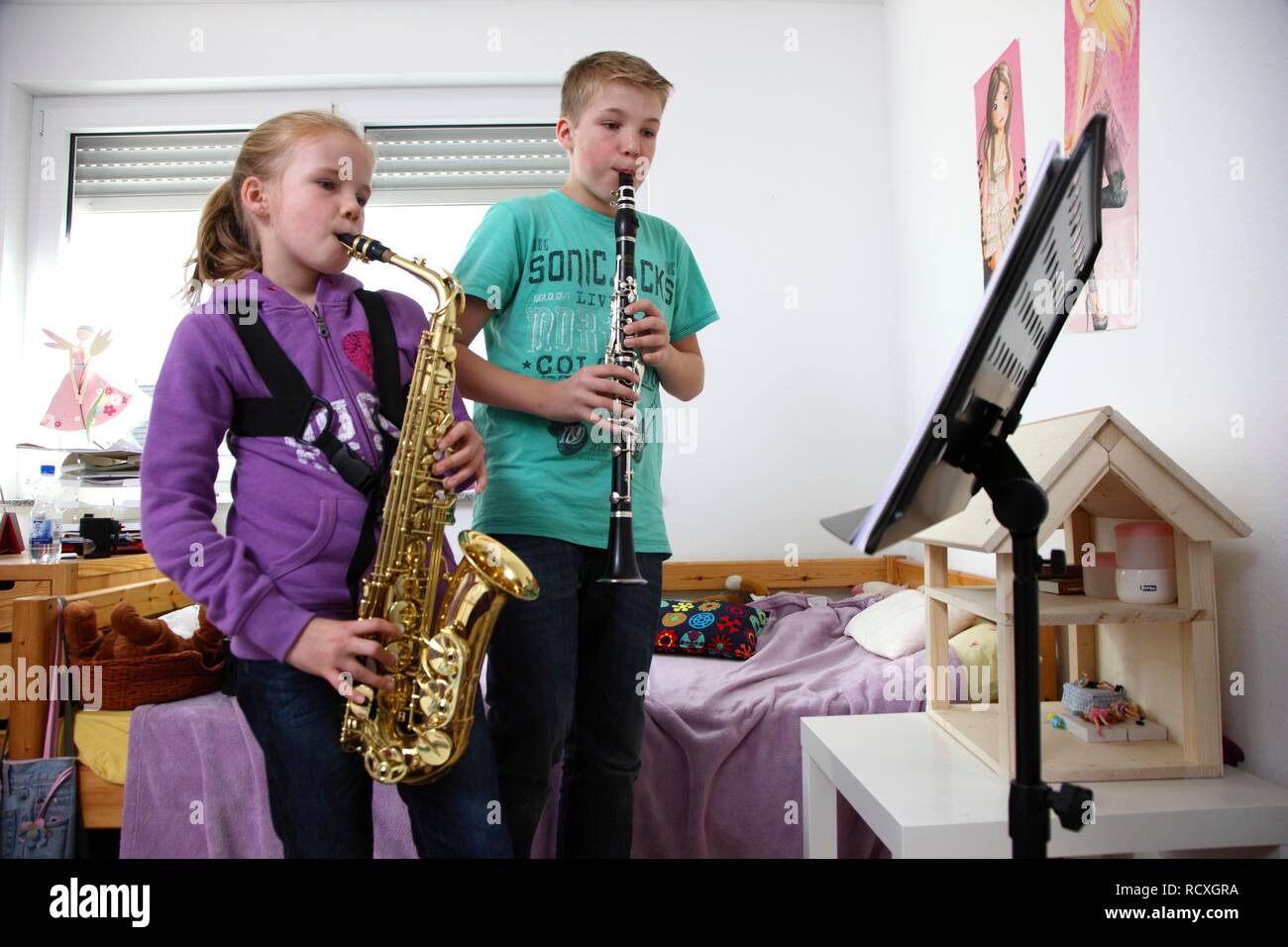 Siblings, a boy, 12 years, and a girl, 10 years, practising clarinet and saxophone in their room Stock Photo