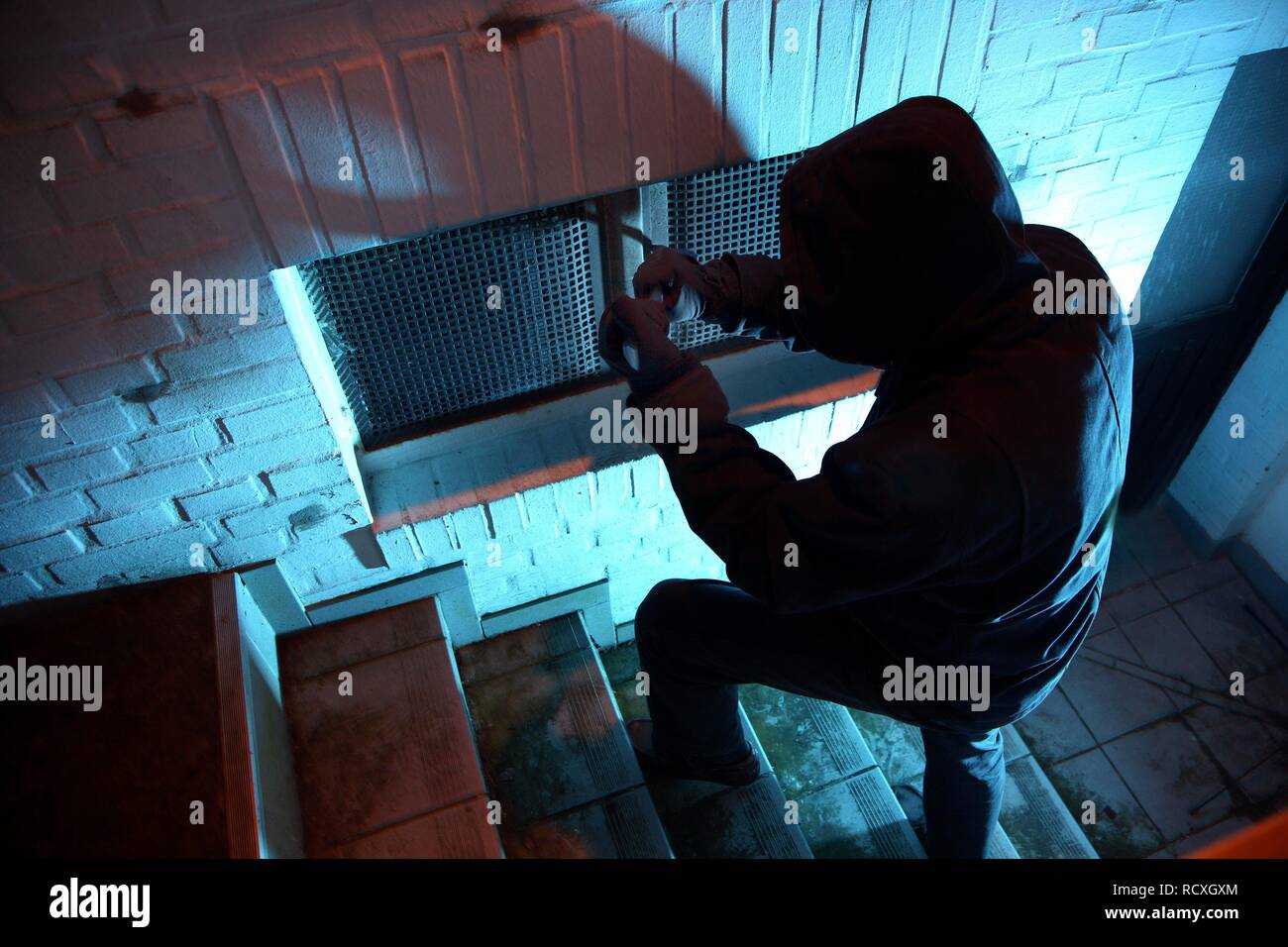 Burglar breaking open cellar window with a crowbar in a cellar corridor, symbolic image for domestic burglary Stock Photo