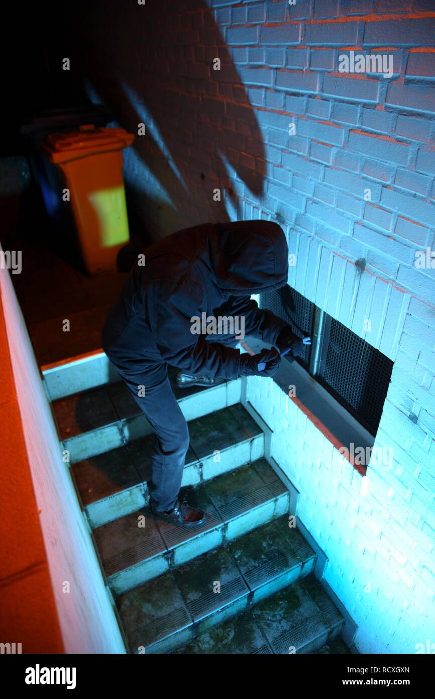 Burglar breaking open cellar window with a crowbar in a cellar corridor, symbolic image for domestic burglary Stock Photo