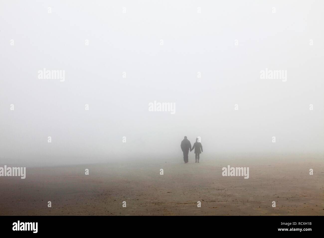 A couple rambling on the beach in fog, autumn, North Sea island of Spiekeroog, Lower Saxony Stock Photo