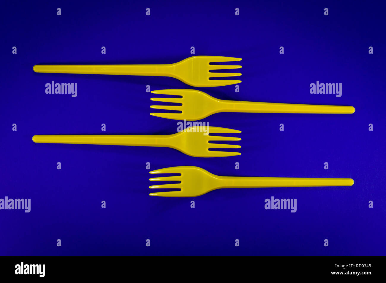 Yellow cutlery plastic forks arrangesd on blue background. Plastic waste problem concep Stock