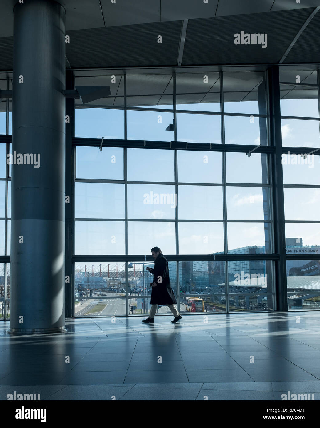 Man walking through terminal looking at phone while leaving Copenhagen airport on way to metro Stock Photo