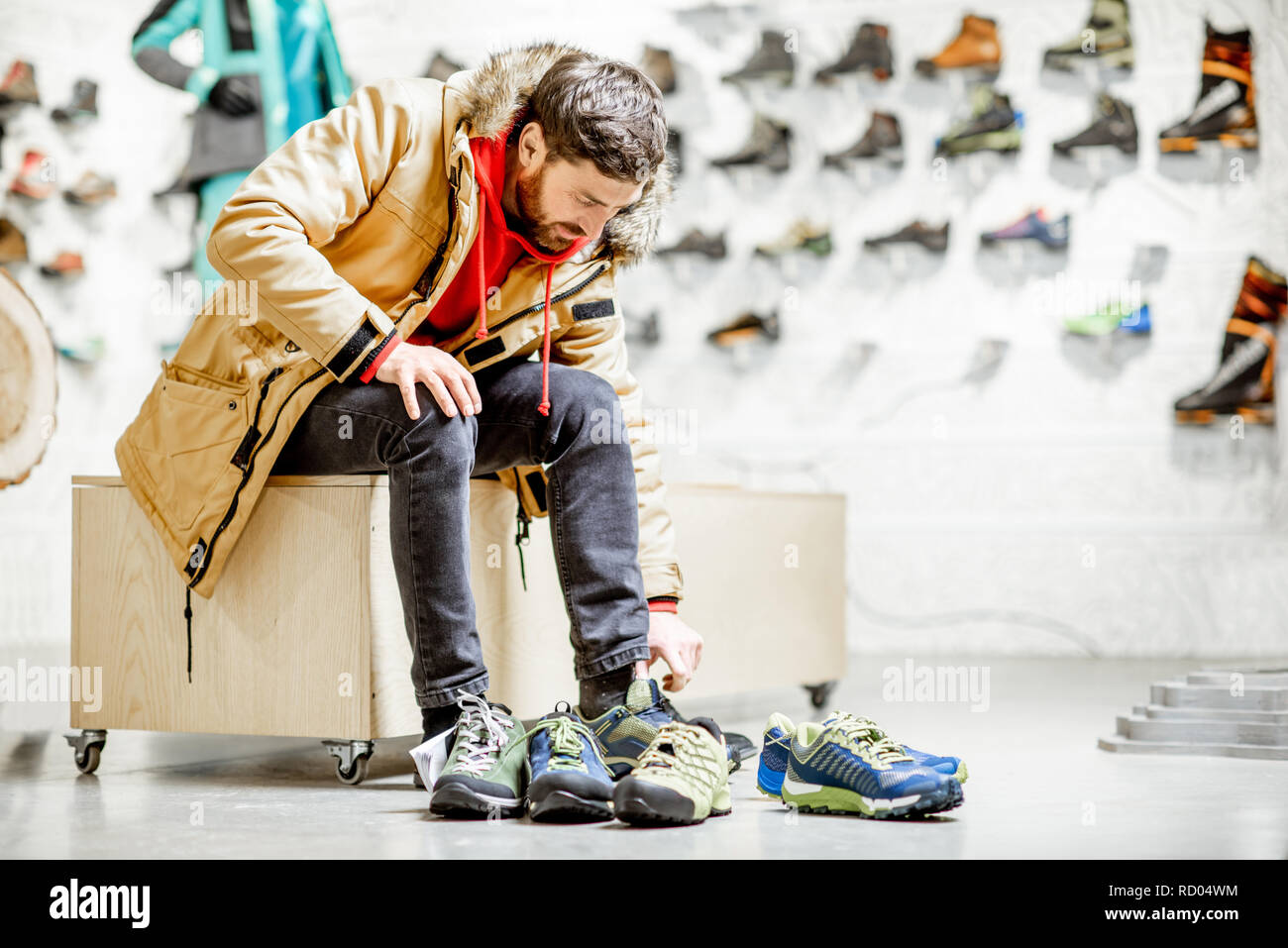 Man in winter jacket trying shoes for mountain hiking sitting in the  fitting room of the modern sports shop Stock Photo - Alamy