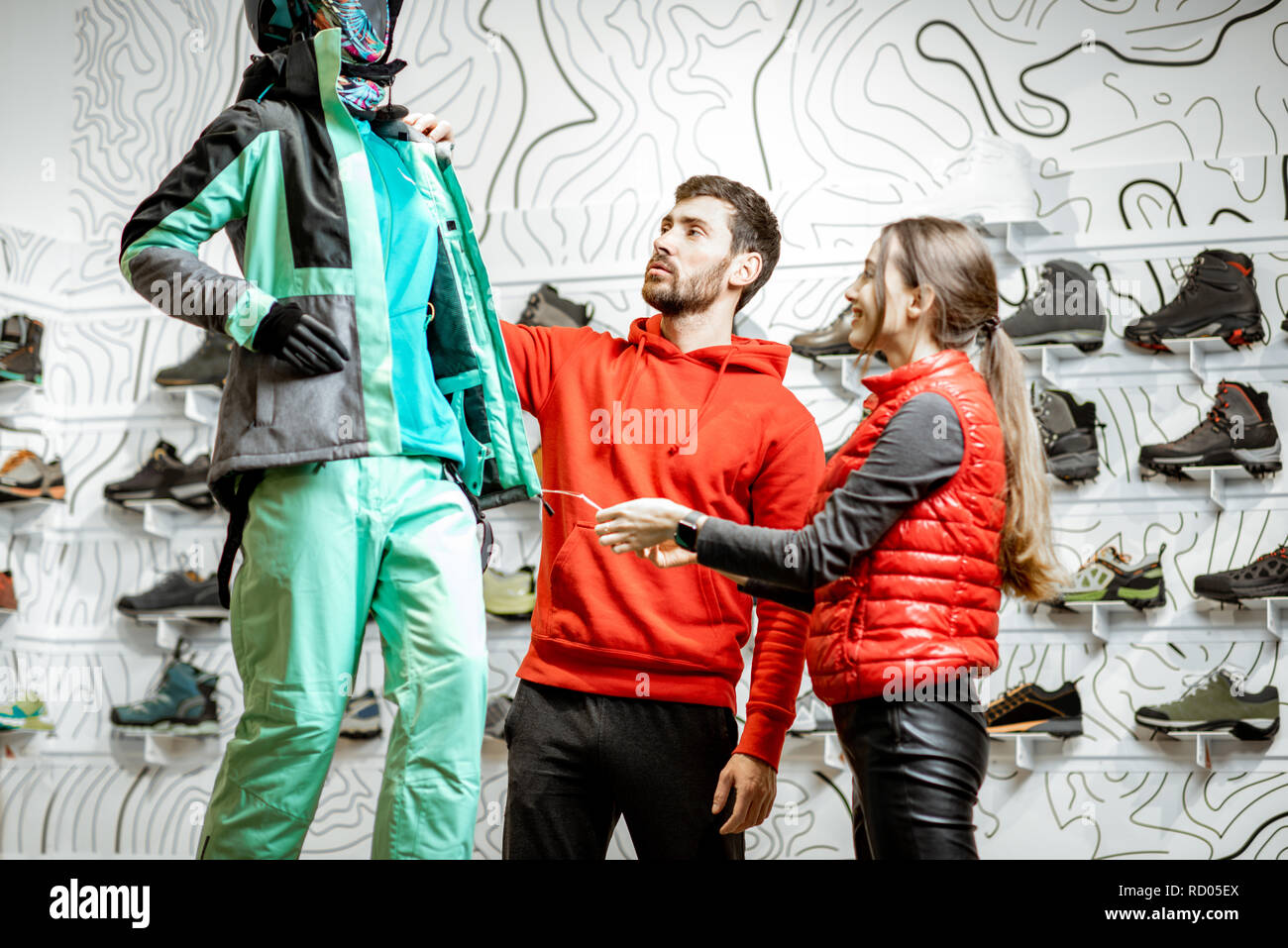 Cheerful couple in red sports clothes choosing ski wear looking on the dummyatn the modern sports shop Stock Photo