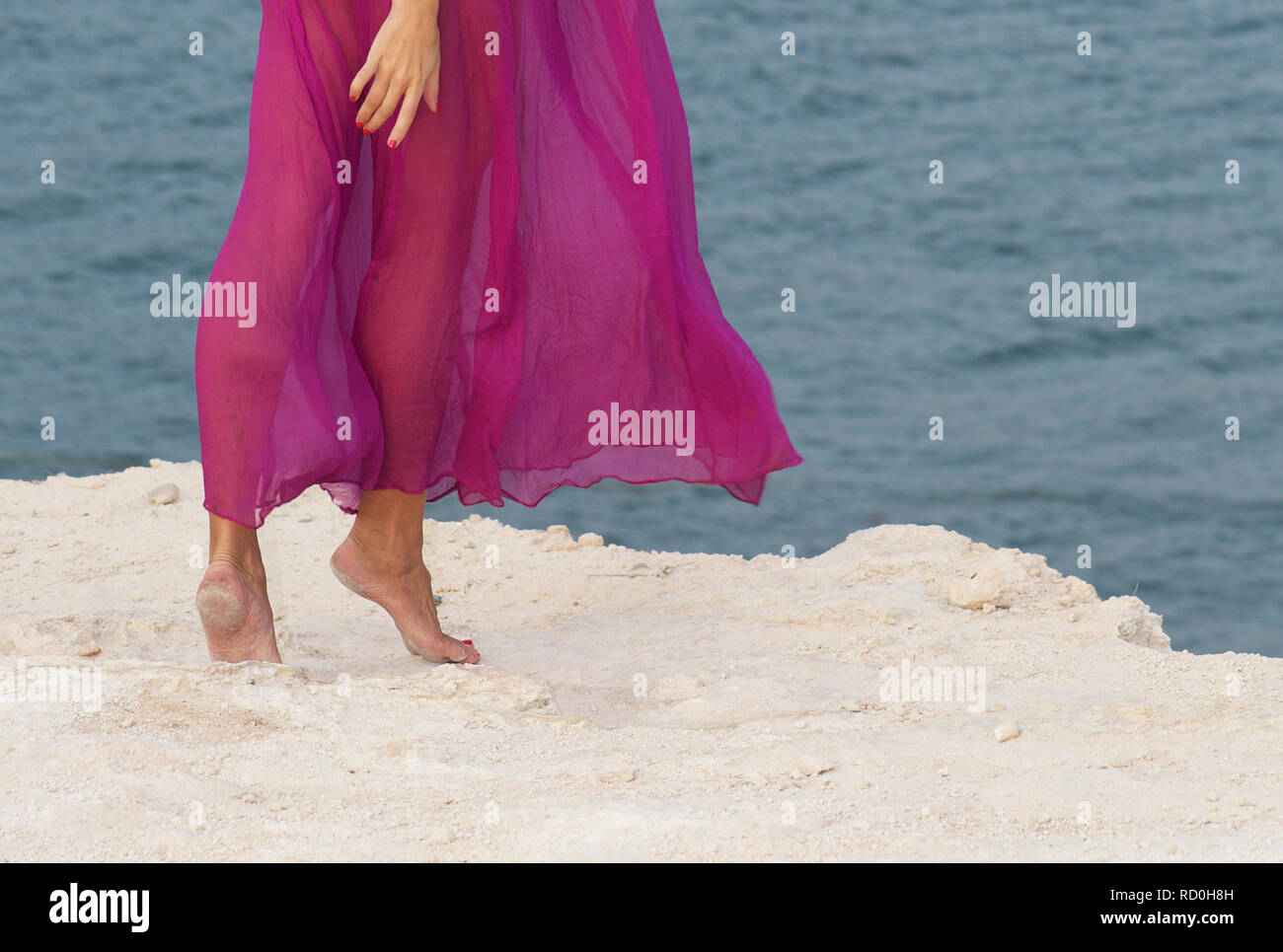 Close-up of a woman's legs standing on beach in a long dress Stock Photo