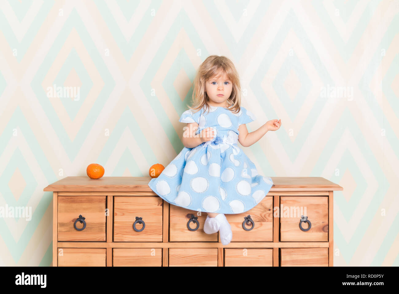 A Little Baby Girl In Her Room Sitting Cross Legged On Chest Of