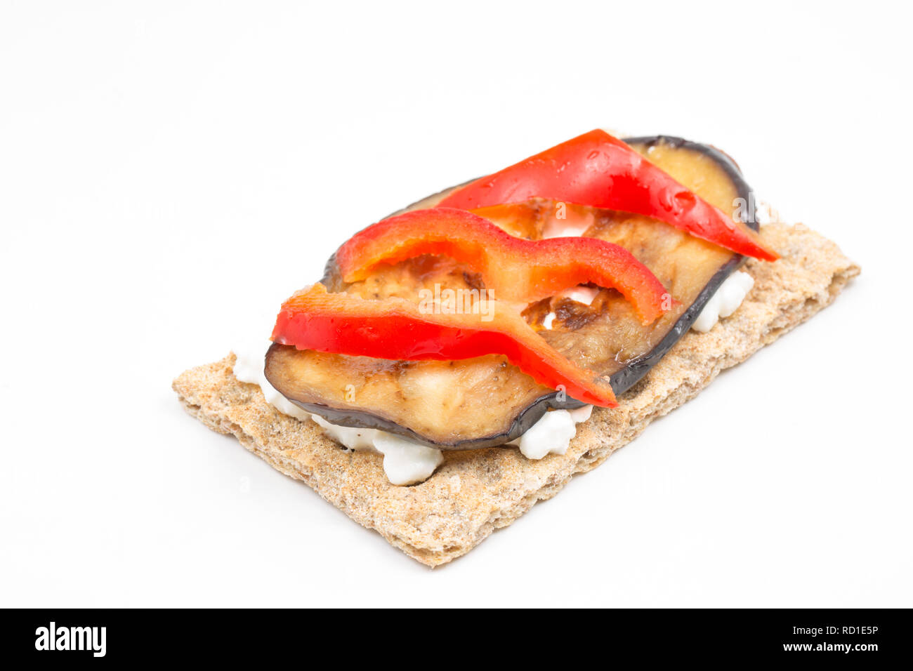 Fat free cottage cheese, spread on a rye bread cracker and topped with fried sliced aubergine and raw red bell pepper as part of a weight loss program Stock Photo