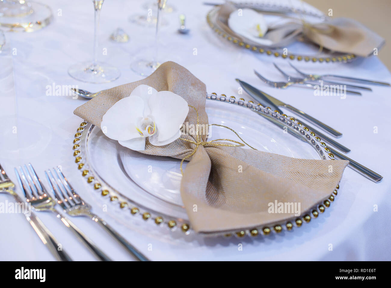 Fine dining table setting featuring transparent plates, beige linen napkin  with natural orchid and golden decorations and shiny silverware Stock Photo  - Alamy