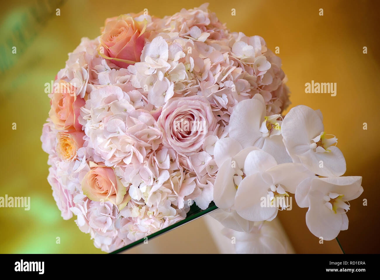 Classy floral arrangement in a pastel round bouquet featuring pink hydrangea roses and orchids, set on an elegant glass support as a centerpiece Stock Photo