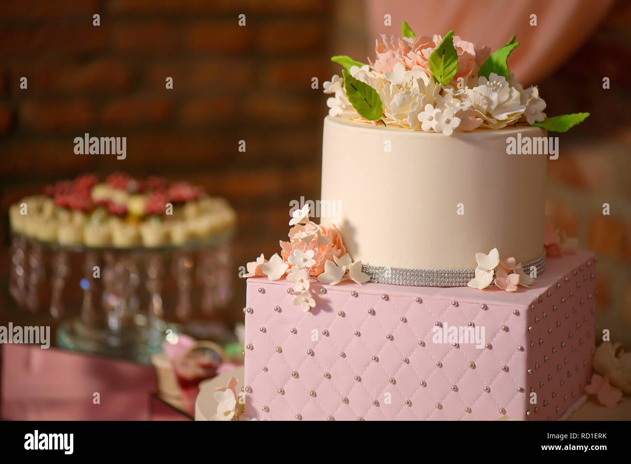 Large assortment of bite-sized cakes and a large three tiered cake embellished with velvet icing and sugar flowers, delicious dessert display Stock Photo