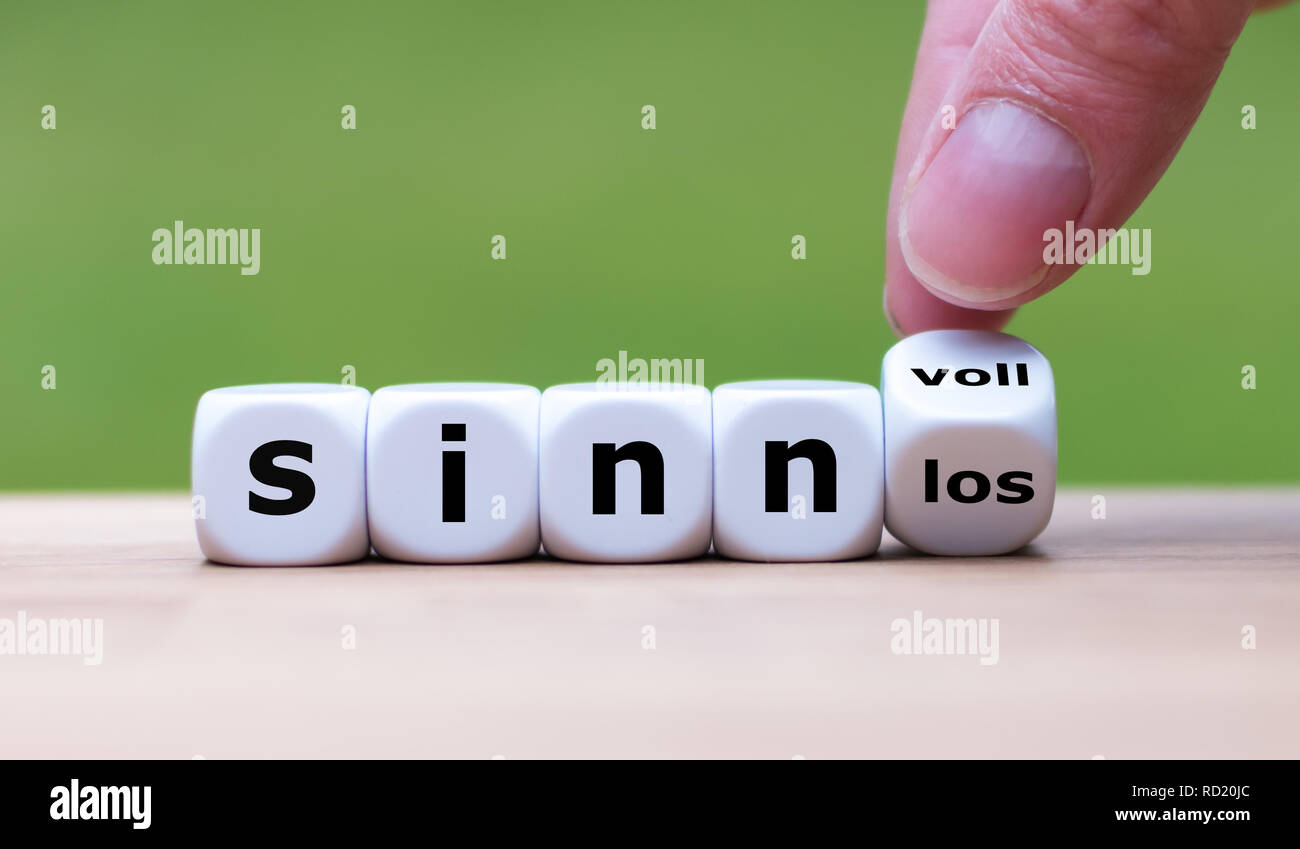 Hand turns dice and changes the german word 'sinnlos' to 'sinnvoll' (meaningless to meaningful) Stock Photo