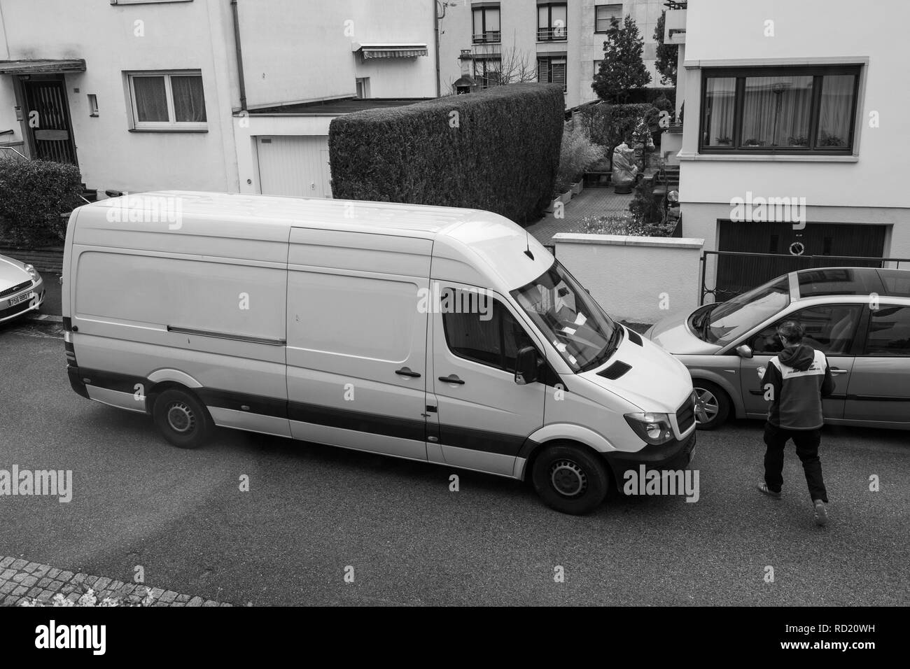 PARIS, FRANCE - MAR 30, 2018: Courier enters DHL yellow delivery van after delivering the on time delivering package parcel in typical European neighborhood - elevated view  Stock Photo