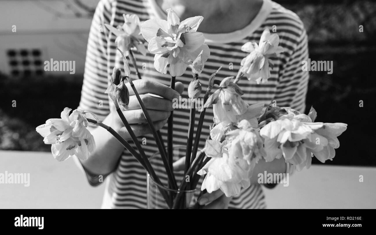 Front view of relaxed woman posing with flower vase with dead narcissus bouquet - black and white image Stock Photo