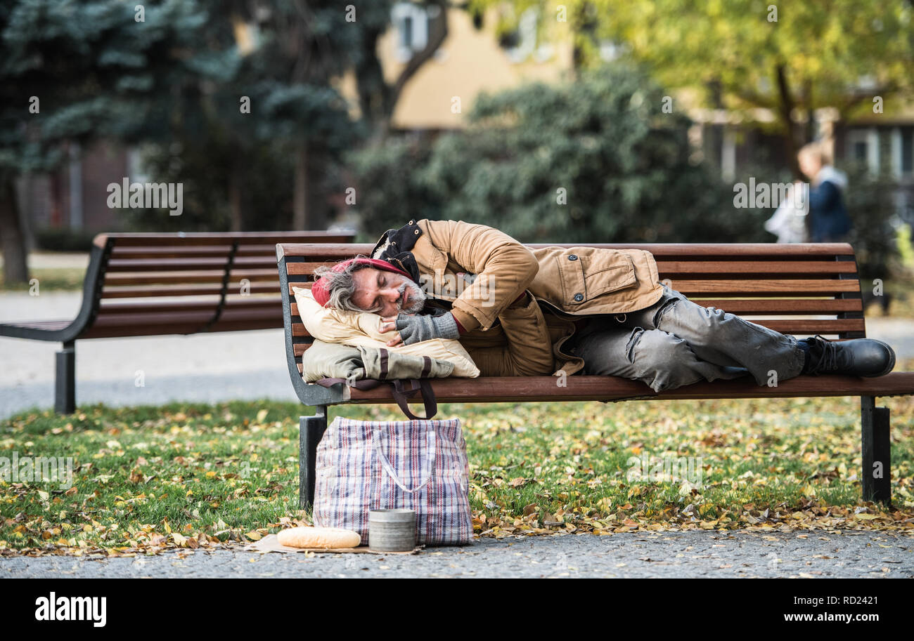 Homeless beggar man with a bag lying on bench outdoors in city, sleeping. Stock Photo