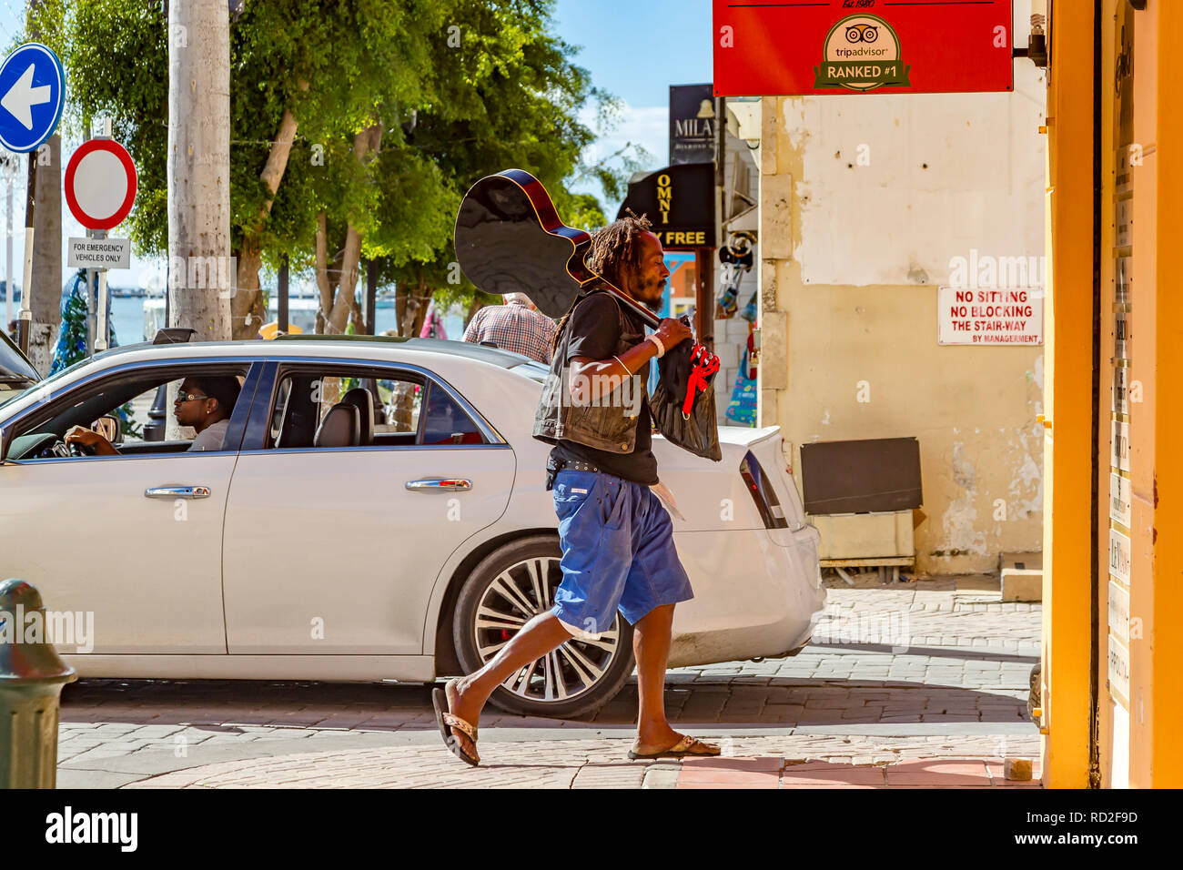 A man carrying a guitar down the cobbled steets in Philipsburg, Sint Maarten. Stock Photo