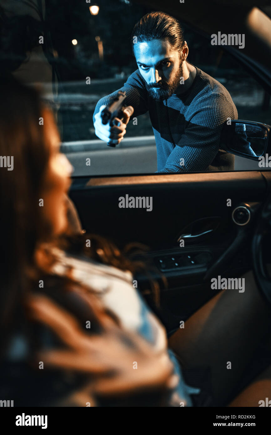 Bandit robberies woman with gun and she is feeling shocked and scared sitting in the car. Stock Photo