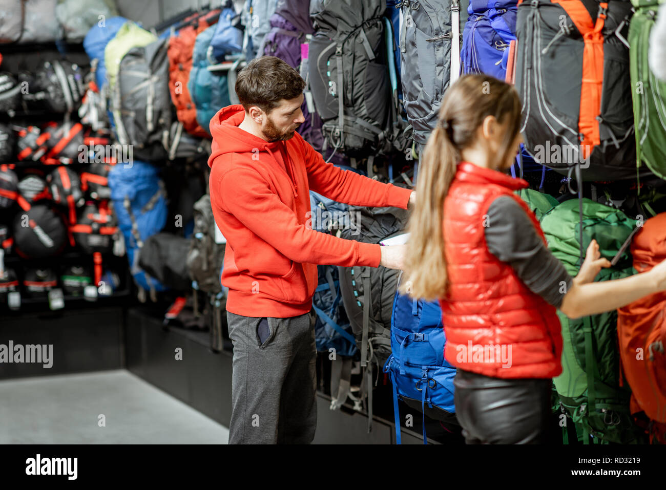 Couple choosing sports equipment looking on the backpacks for traveling in the shop Stock Photo