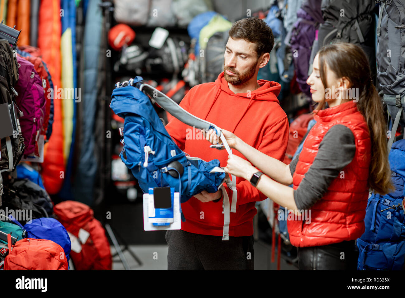 Couple choosing sports equipment looking on the backpacks for traveling in the shop Stock Photo
