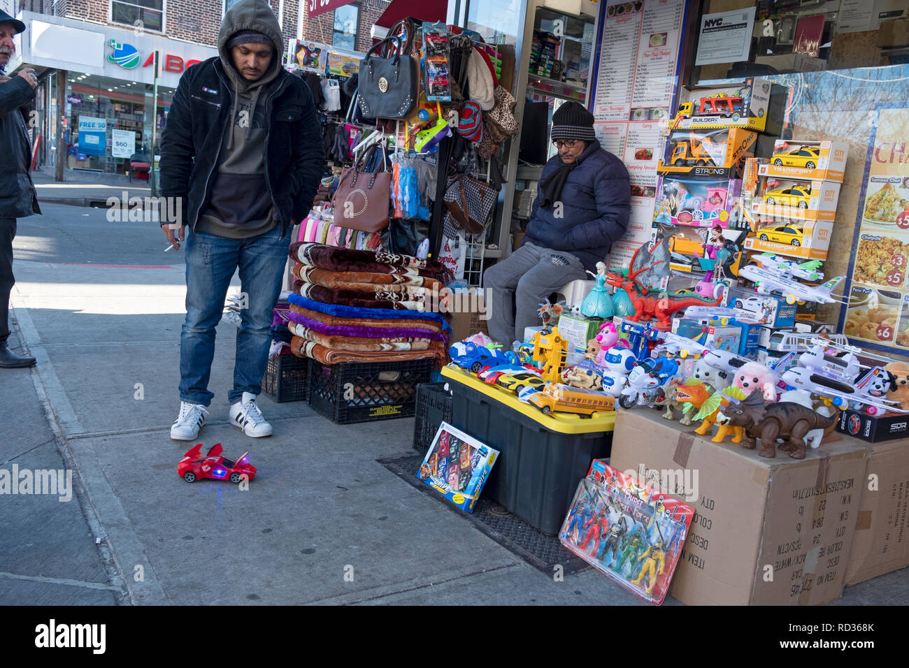 A street scene in Jackson Heights, Queens with a merchant and a young man looking a t a wind-up race car. Stock Photo