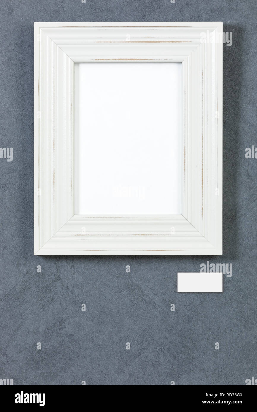 White wooden frame on grey painted wall, picture area isolated with clipping path. Blank caption plate and copy space below Stock Photo