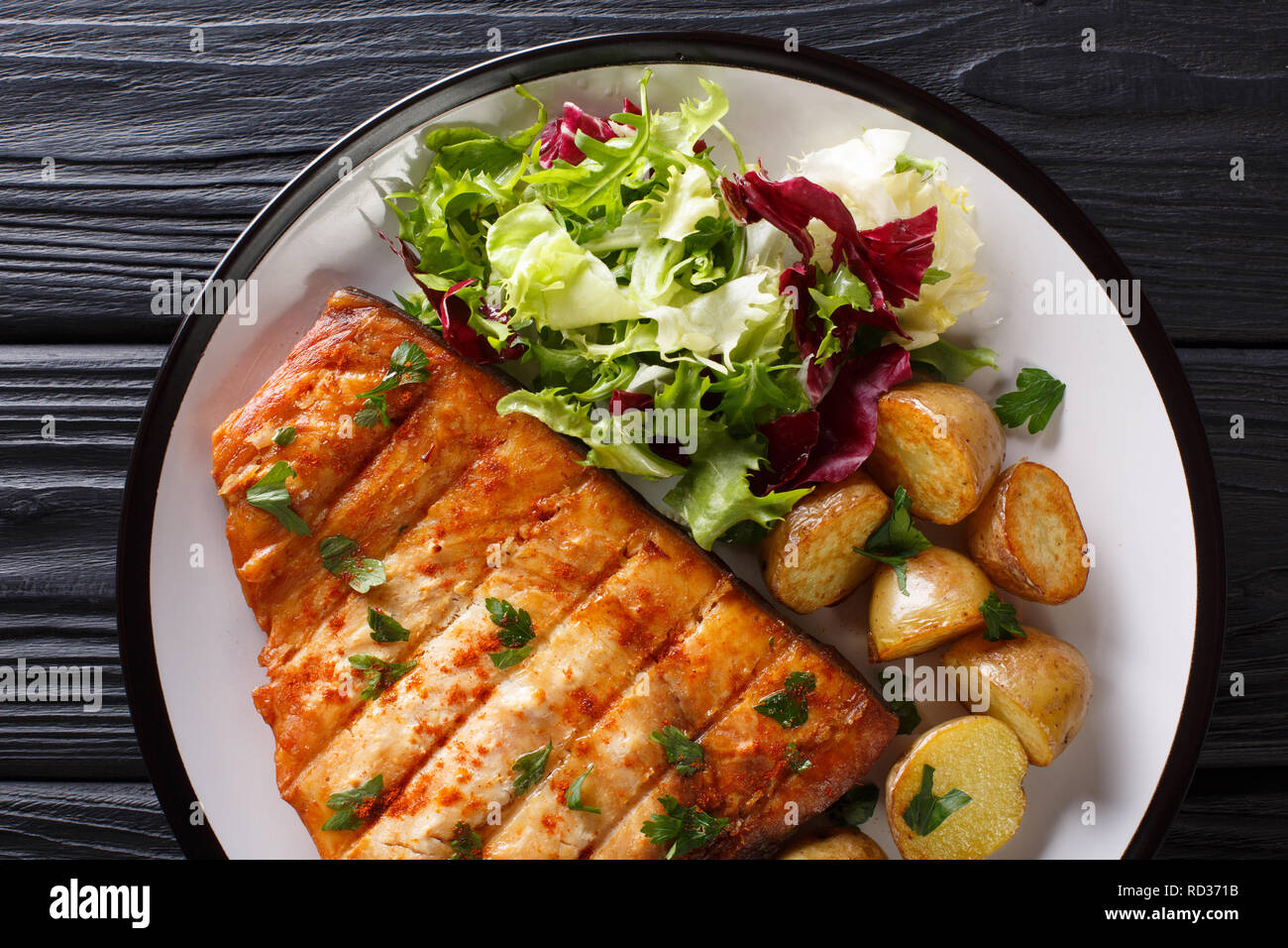 Grilled swordfish fillet with fried potatoes and fresh salad close-up on a plate on a wooden table. horizontal top view from above Stock Photo
