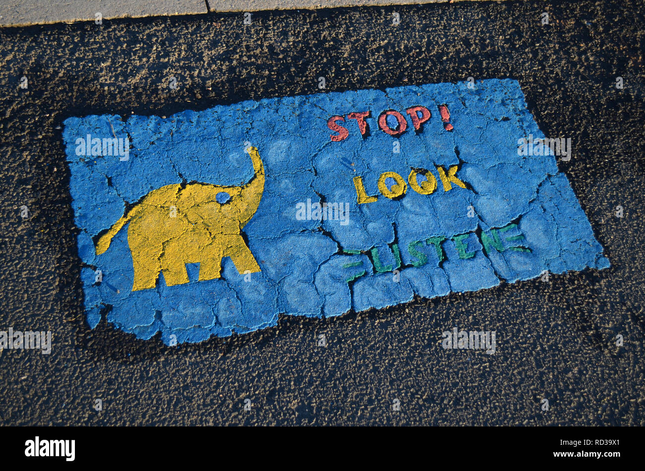 Weathered sign on the pavement for children to read, Stop, Look, Listen, with a yellow elephant. Stock Photo