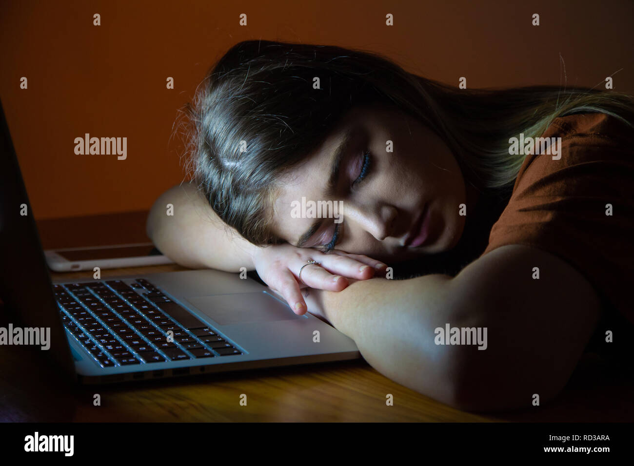 A teenage girl asleep with her head resting on the desk in front of her laptop. Stock Photo
