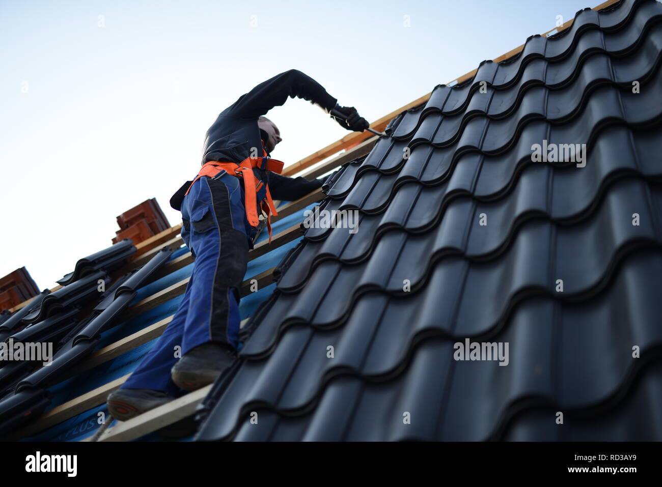 Dach neu mit schwarzen Dachsteinen eindecken. Dachdecker mit Werkzeug in Deutschland, Handwerker Bauarbeiter in Berlin im Herbst Stock Photo