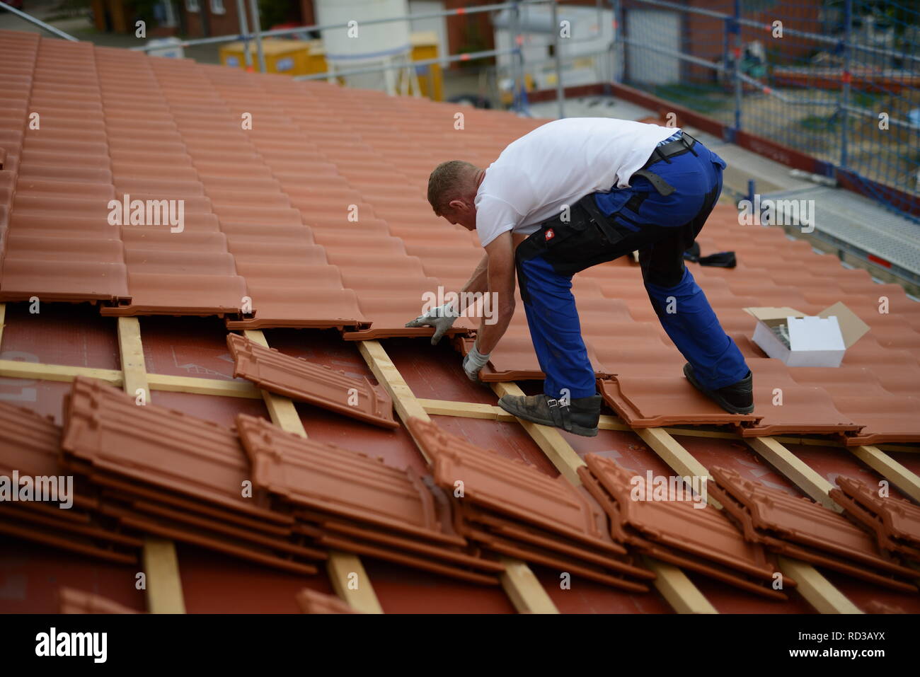 Dach Baustelle neu mit roten Dachziegeln. Dachdecker Bauarbeiter in weißem T-Shirt und Arbeitshandschuhen in Deutschland. Mann bei der Arbeit. Stock Photo